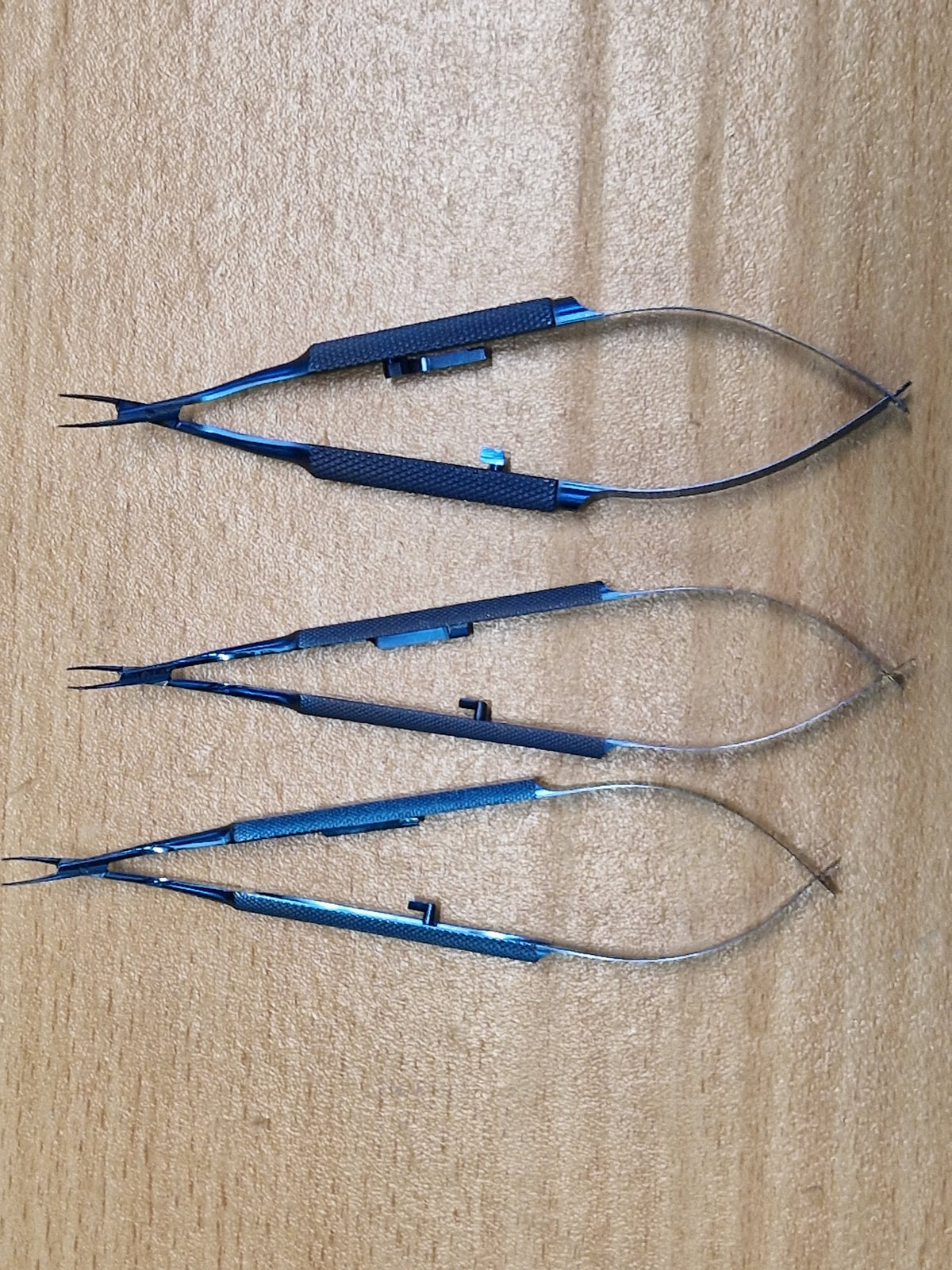 Three blue titanium Castroviejo-style ophthalmic micro needle holders with locking spring handles
